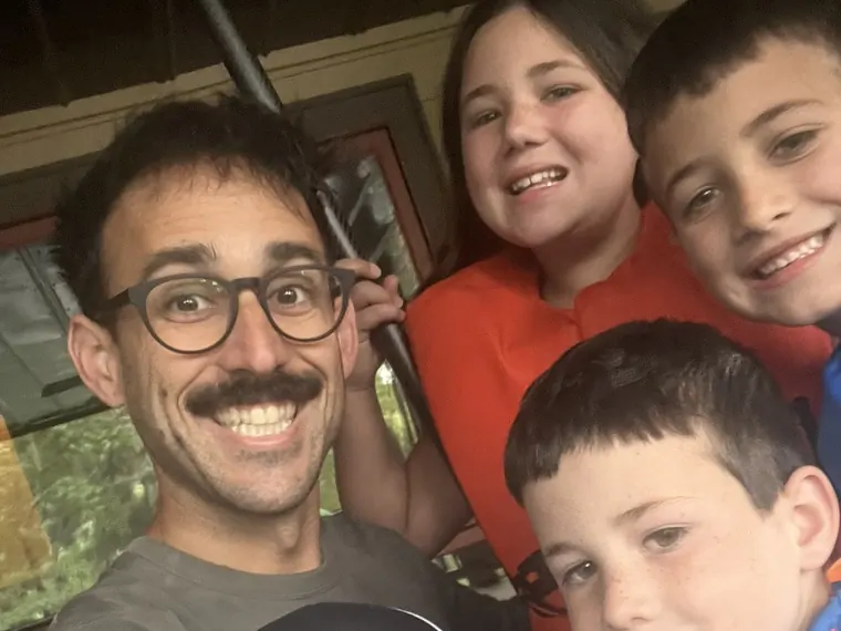 Danny grinning in a close selfie with four laughing kids crowded in around him